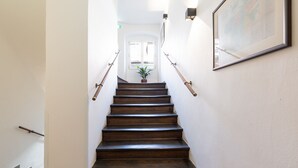 Una escalera de madera con barandillas, que lleva a una puerta con una planta en maceta en la parte superior.