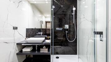 Un baño moderno con ducha envuelta en vidrio, un lavamanos blanco y un salpicadero de mármol negro.