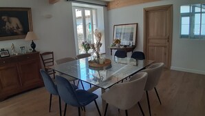 A dining area with a glass table, blue and beige chairs, a wooden cabinet, and a painting on the wall.