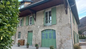 A rustic stone building with green shutters and potted plants in front.
