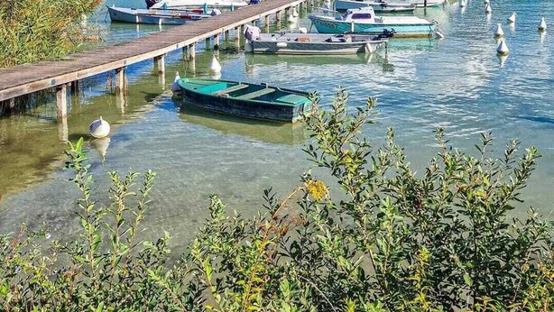 A marina with boats docked along a wooden pier, surrounded by mountains and clear water.
