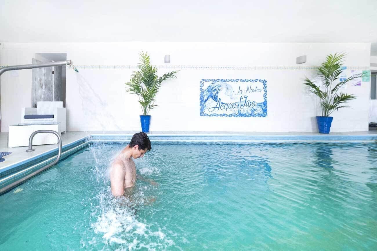 A swimming pool with a person in the water, a shower area, and potted plants.