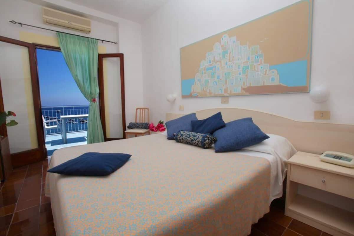 Ein Hotelzimmer mit einem Bett, einem Nachttisch, einem Gemälde und Meerblick.
