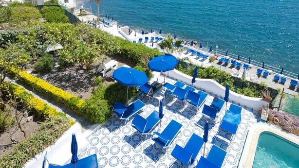 A resort with a pool area, lounge chairs, and a view of the sea.