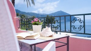 A balcony with a view of the sea, a potted plant, and an open book.