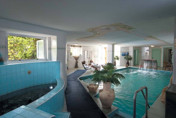 Une piscine intérieure avec un jacuzzi, un espace détente et une vue sur l’extérieur.