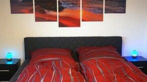 A bedroom with a bed, a nightstand, and a wall with three sunset paintings. - Modern vacation apartment in a quiet location (Meißner)