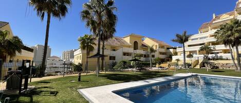 A resort with a swimming pool, palm trees, and multi-story buildings with balconies.