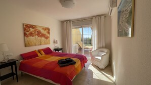 Hotellihuone, jossa on sänky, tuoli, taulu ja ikkuna, jossa on verhot.