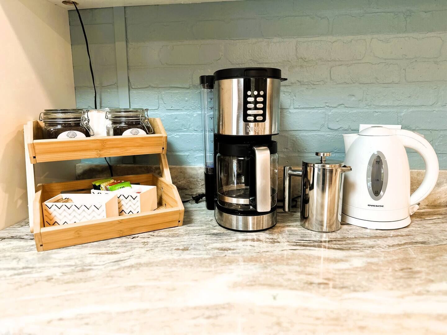A kitchen counter with a coffee maker, a kettle, and a wooden storage unit with jars and boxes.