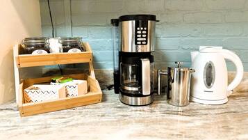 A kitchen counter with a coffee maker, a kettle, and a wooden storage unit with jars and boxes.