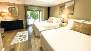 A hotel room with two beds, a dresser, a mirror, a window with a view of greenery, and a beach-themed wall art. - 🐚Shell City on Lt Island (Wellfleet)