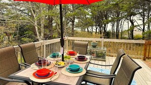 A deck with a table set for dining, surrounded by chairs, and an umbrella providing shade. - 🐚Shell City on Lt Island (Wellfleet)