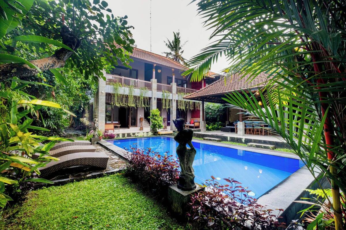A pool surrounded by lush greenery, a building with a tiled roof, and a statue.