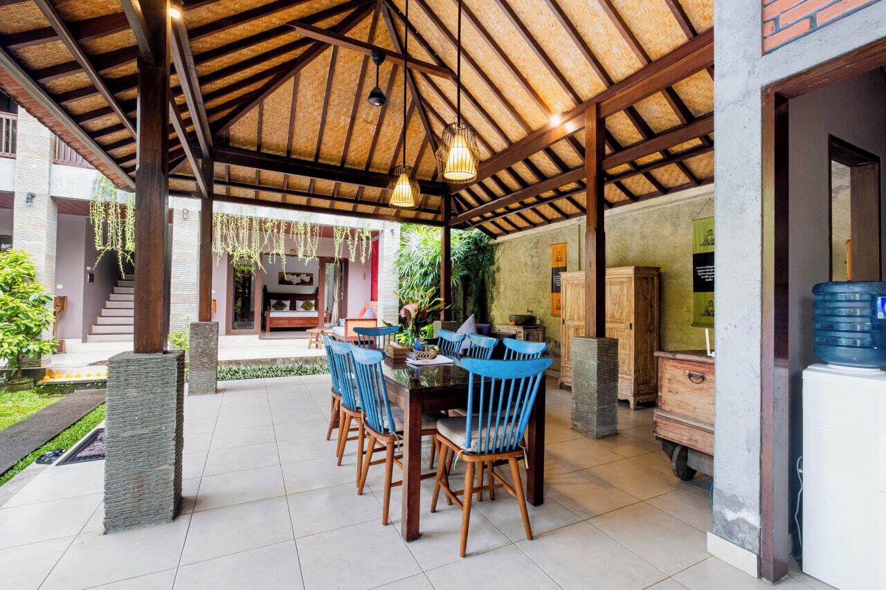 Un área de comedor al aire libre con techo cubierto, sillas de madera y luces colgantes.