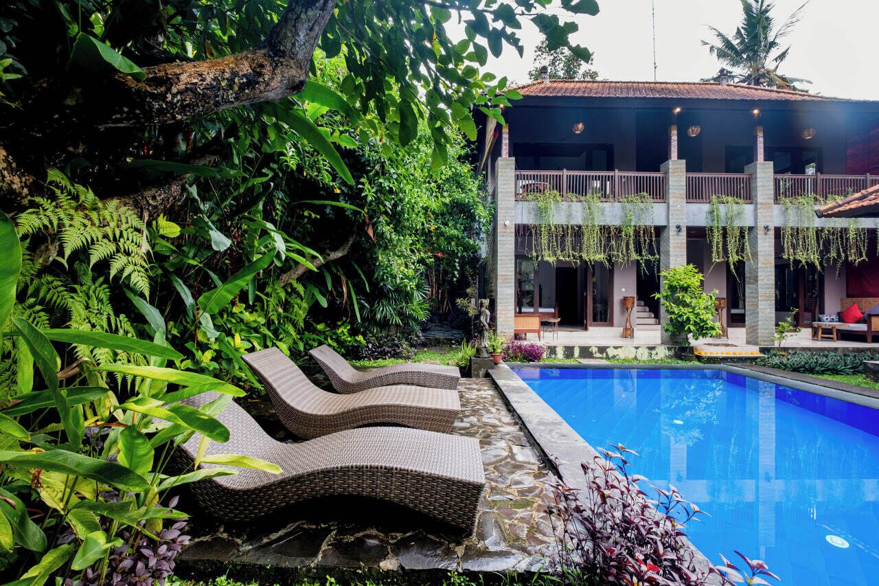 A poolside area with lounge chairs, a pool, and lush greenery.