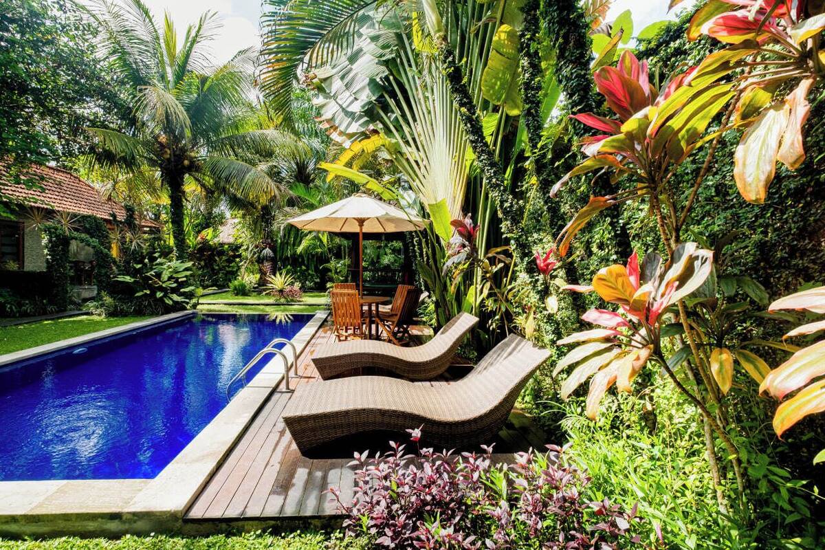 A pool with lounge chairs and a table, surrounded by lush tropical plants.