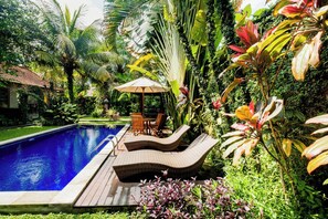 Una piscina con sillones de descanso y una mesa, rodeada de exuberante vegetación tropical.