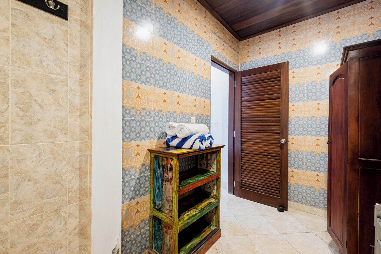 A bathroom with patterned tiles, a wooden door, and a shelf with towels.
