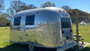 A silver trailer with a reflective surface, a license plate, and a roof-mounted air conditioning unit.