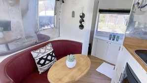 A compact kitchen with a red cushioned seating area, a small wooden table, and a window with a view of the outside.