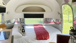 A cozy interior with a bed, a small table, and a window offering a view of greenery.
