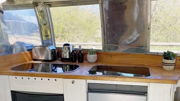 A compact kitchen with a wooden countertop, stainless steel sink, and a window providing a view of greenery outside.