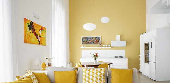 Un salon moderne avec un mur jaune, des meubles blancs et des œuvres d’art.