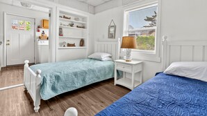 A room with two beds, a white wardrobe, a small white nightstand, and a window with blinds.