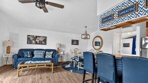 A living room with a blue sofa, wooden coffee table, and a dining area with blue chairs.
