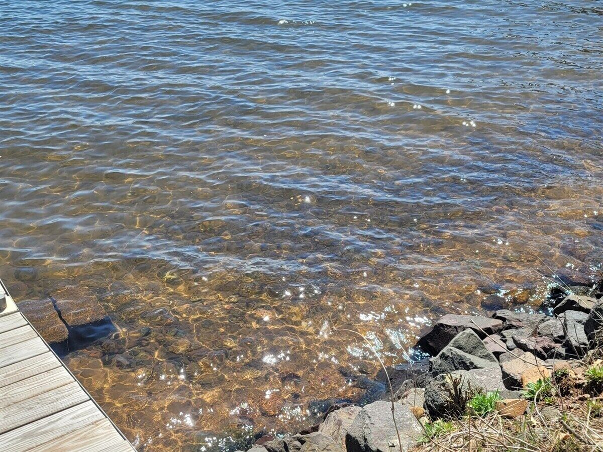 A wooden dock extending into clear, shallow water with visible rocks and pebbles at the edge.