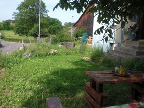 A rustic outdoor setting with a wooden table and benches, surrounded by greenery and a stone building. - Gite Rural, restaurant without alcohol/pork (Beurnevésin)