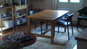A dining area with a wooden table and chairs, a television mounted on the wall, and a window with blinds. - Gite Rural, restaurant without alcohol/pork (Beurnevésin)