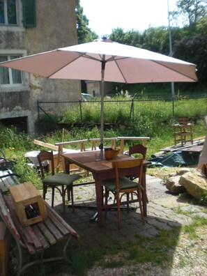 An outdoor patio with a table and chairs, an umbrella, and a rustic building in the background. - Gite Rural, restaurant without alcohol/pork (Beurnevésin)