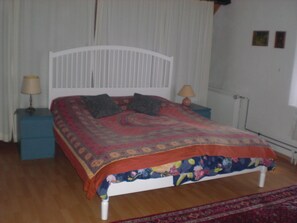 A bedroom with a white bed, two bedside tables, a red and blue floral bedspread, and a red rug. - Gite Rural, restaurant without alcohol/pork (Beurnevésin)