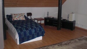 A bedroom with a bed, a chair, a small table, a radiator, and a speaker. - Gite Rural, restaurant without alcohol/pork (Beurnevésin)
