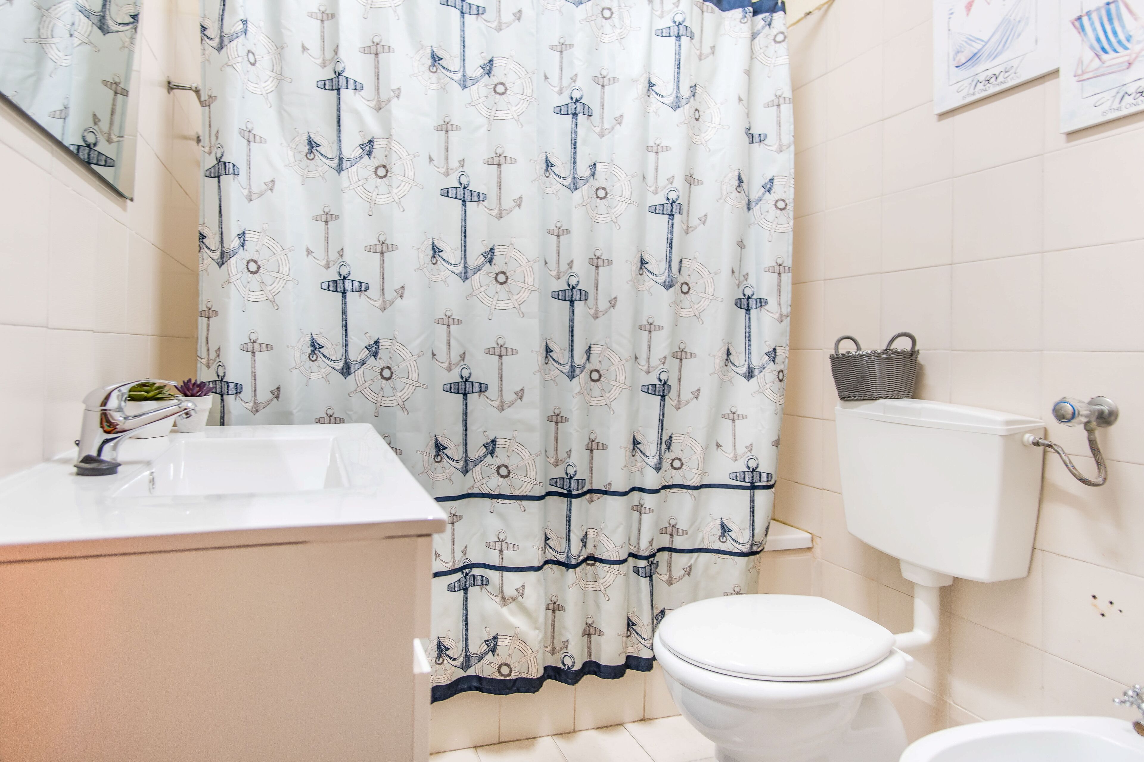 Een badkamer met een wit toilet, een wastafel met een moderne kraan en een douchegordijn met een ankerprint.