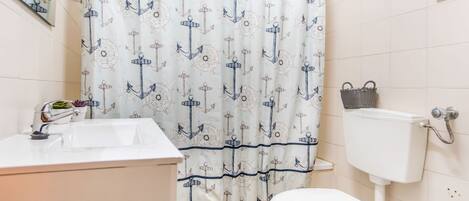 Een badkamer met een wit toilet, een wastafel met een moderne kraan en een douchegordijn met een ankerprint.