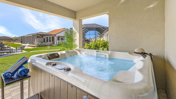 A hot tub on a covered patio with a view of houses and a lawn. - The Charm of a sand castle, creative & artisitc, Waterfront - Villa Sand Castle - Roelens Vacations (Cape Coral)