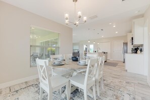 A modern kitchen with white cabinetry, a dining area with white chairs and a round table, and a chandelier. - The Charm of a sand castle, creative & artisitc, Waterfront - Villa Sand Castle - Roelens Vacations (Cape Coral)