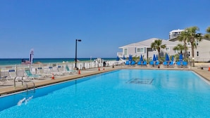 Una piscina con sillones reclinables y sombrillas, una bandera y un edificio con vista al océano.