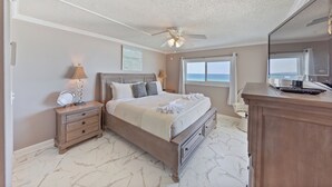 Un dormitorio con cama, mesitas de noche, ventilador de techo, ventana con vistas y cómoda.