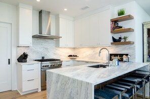 Une cuisine moderne avec des meubles blancs, un îlot en marbre, une cuisinière à gaz et un four encastré.