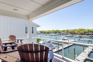Un balcon doté de mobilier en bois, donnant sur une marina où sont amarrés des bateaux.