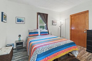 A bedroom with a bed, a nightstand, a dresser, a lamp, and a door.