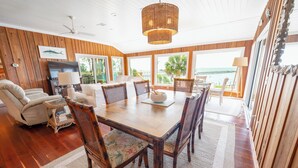 Un comedor con mesa de madera, sillas y vista al océano.
