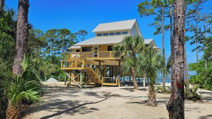 Un edificio de dos pisos con balcón, rodeado de árboles y una playa.