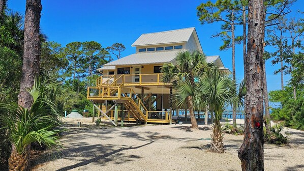 A two-story building with a balcony, surrounded by trees and a beach. - BAYFRONT - Old Florida Style Cottage w/ private dock! (St. George Island)
