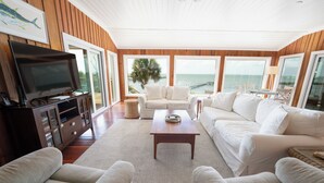 Una sala de estar con televisor, sofá, mesa de centro y grandes ventanas con vista al mar.