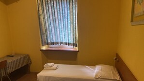A small hotel room with two single beds, a table with a striped tablecloth, and a window with patterned curtains.